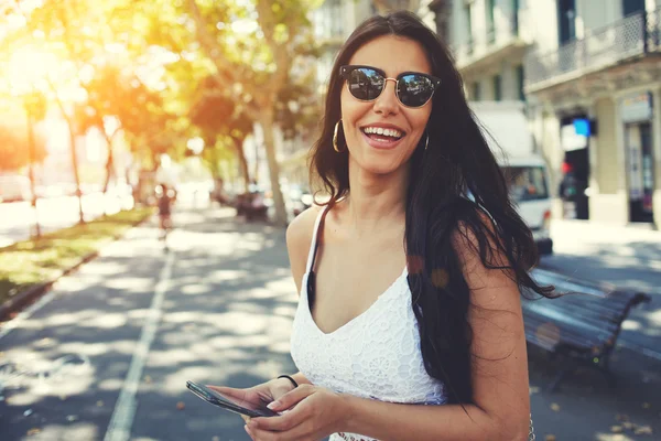 Latin woman in sunglasses using smartphone