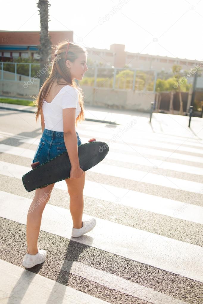 Woman with longboard crosses the road