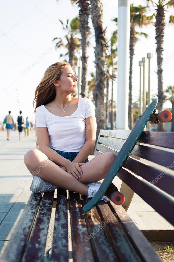 Woman with penny board sitting on a bench