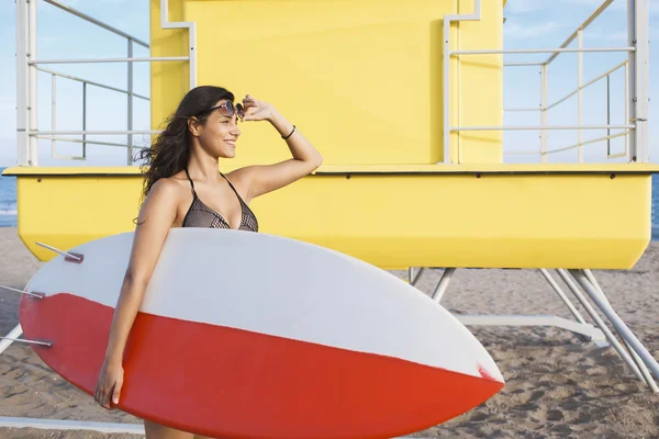 Mujer de pie con tabla de surf cerca de la casa de salvavidas — Foto de Stock