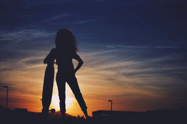 Silhouette of woman standing with her longboard