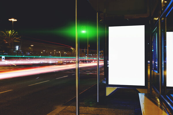 Blank electronic billboard with copy space for your text message or content, public information board on bus stop in the big city at night, advertising mock up with movement of cars on the background