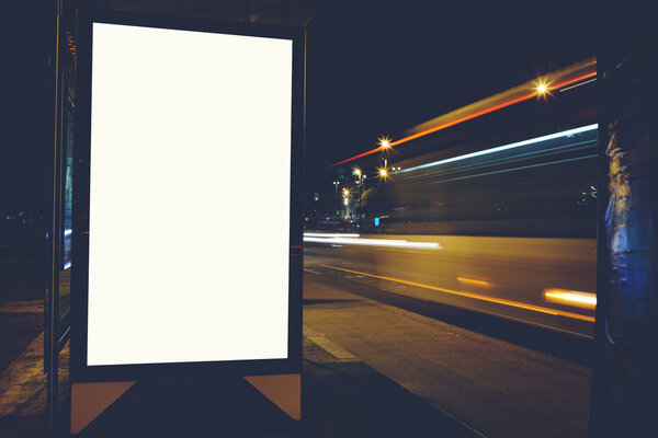 Illuminated empty billboard with copy space for your text message or content, public information board with blurred night lights on background, advertising mock up in outside, blank poster on roadside