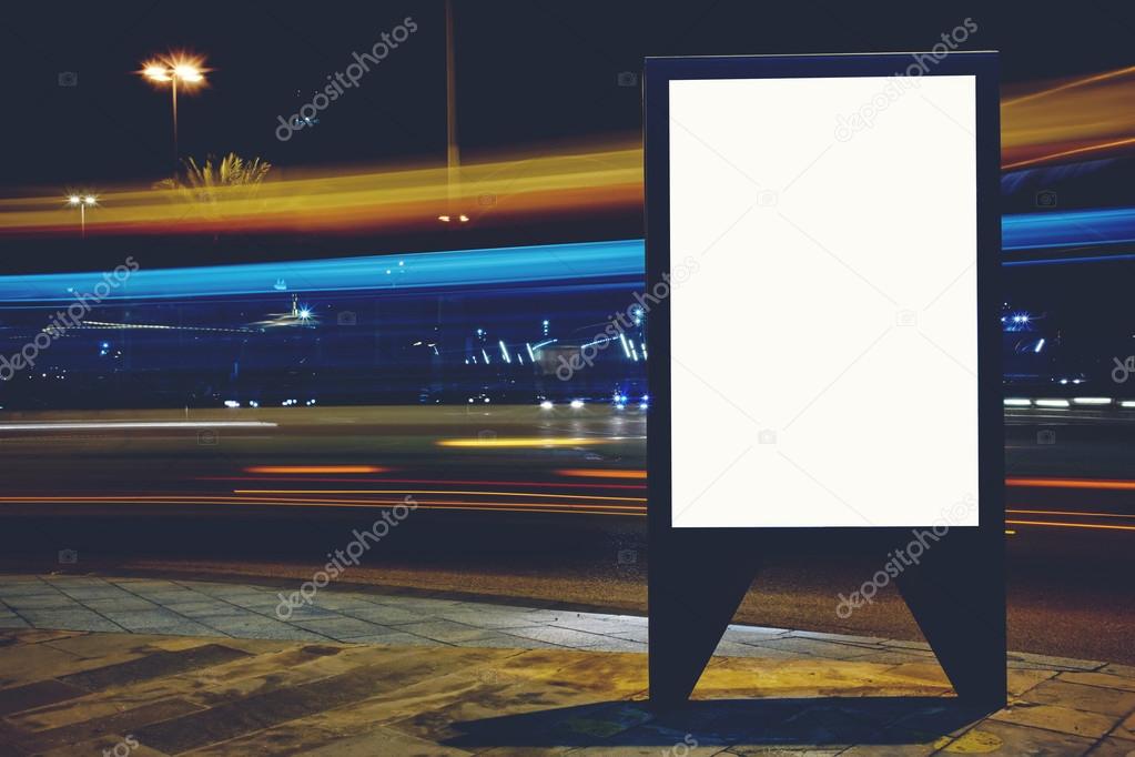 Illuminated blank billboard with copy space for your text message or promotional content, advertising mock up banner on roadside in night, public information board with blurred vehicles on high speed