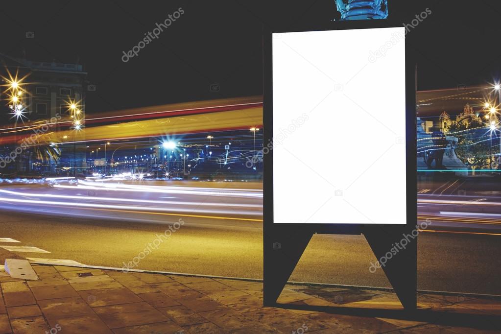 Illuminated blank billboard with copy space for your text message or content, public information board with shutter speed on background, advertising mock up outside, empty poster on roadside