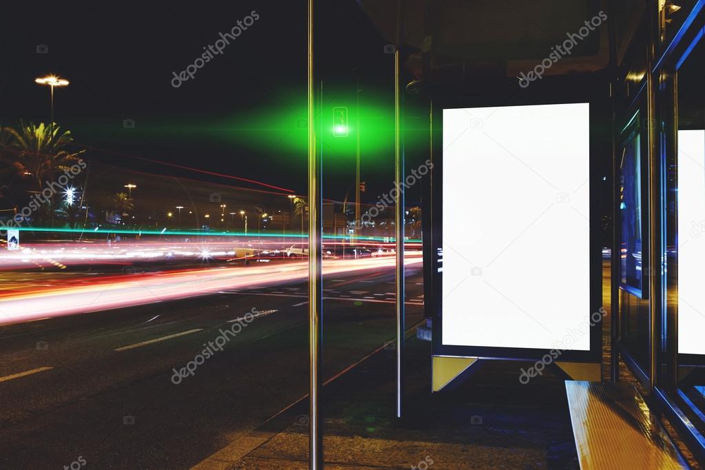 Blank electronic billboard with copy space for your text message or content, public information board on bus stop in the big city at night, advertising mock up with movement of cars on the background