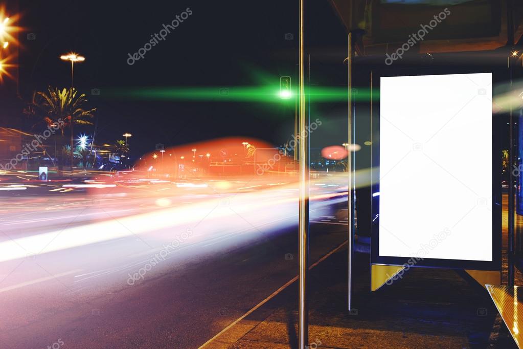 Illuminated blank billboard with copy space for your text message or content, public information board with blurred cars lights on background, advertising mock up outdoors, empty Lightbox on bus stop