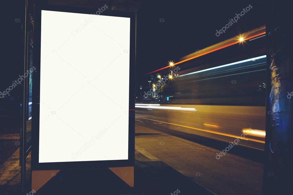 Illuminated empty billboard with copy space for your text message or content, public information board with blurred night lights on background, advertising mock up in outside, blank poster on roadside