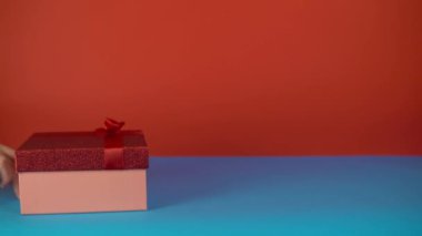 Arkadaşlarına tatil hediyesi ver, kırmızı ve mavi arka planda hediyeyle elini yudumla.