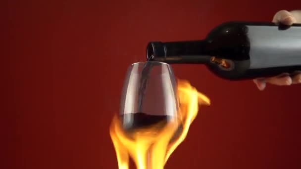 Verter vino tinto en el vaso de la botella, quemar la copa de vino en el fuego sobre el fondo — Vídeos de Stock