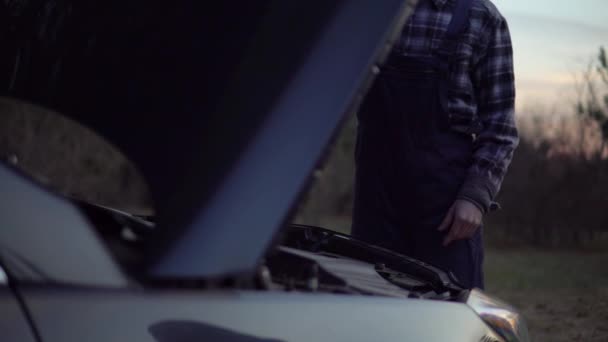 Мечанин в униформе открыл капот мотора и починил разбитую машину на дороге — стоковое видео
