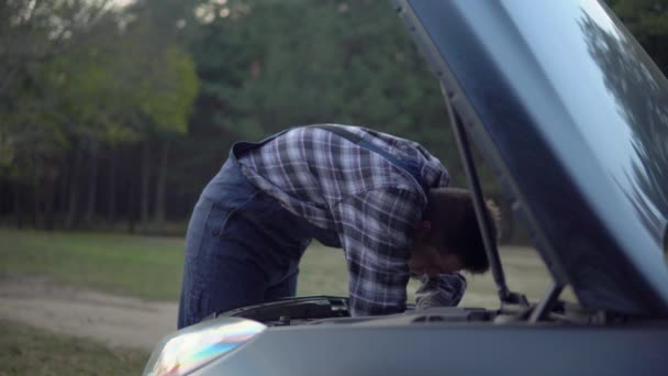 İş üniformalı tamirci açık kaput motoru orman yolunda bozuk araba tamir ediyor. — Stok video