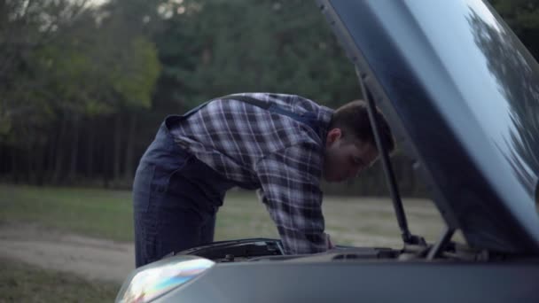 Araba tamircisi bozuk arabayı tamir ediyor, açık kaputun altına bakıyor. Arızalı araba yolda. — Stok video