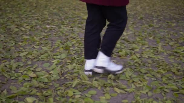 Vrouw die buiten over omgevallen boombladeren loopt. vrouw in wit shoes close up — Stockvideo