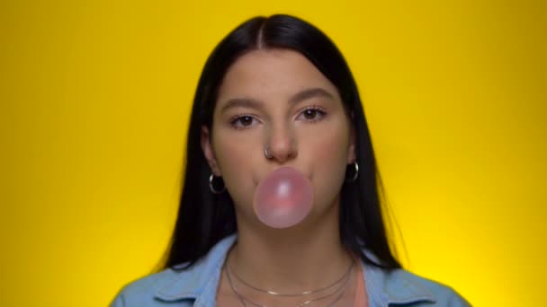 Smiling woman looking at camera, chawing blowing pink bubble gum, slow motion — Stockvideo