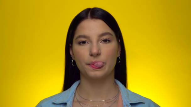 Kvinna blåser tuggummi och tittar in i kameran. Kvinna på gul bakgrund — Stockvideo
