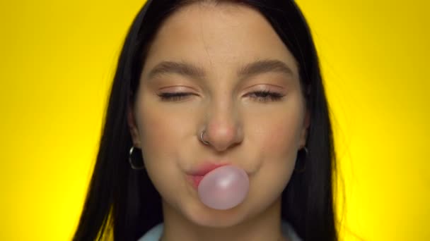 Attractive woman looking at camera and blowing bubble gum on yellow background — Stock Video