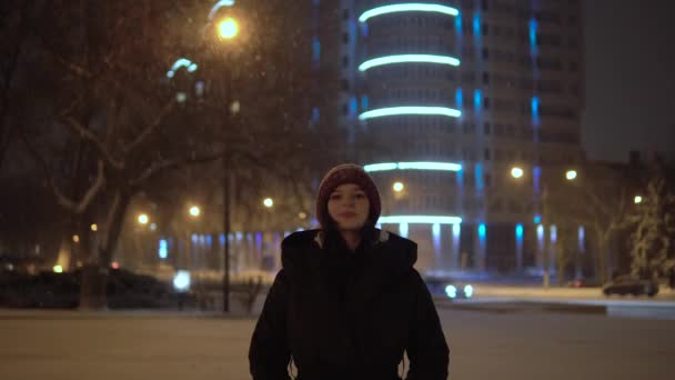 Una mujer atractiva mirando la cámara. Invierno caminando por la calle durante las nevadas — Vídeos de Stock