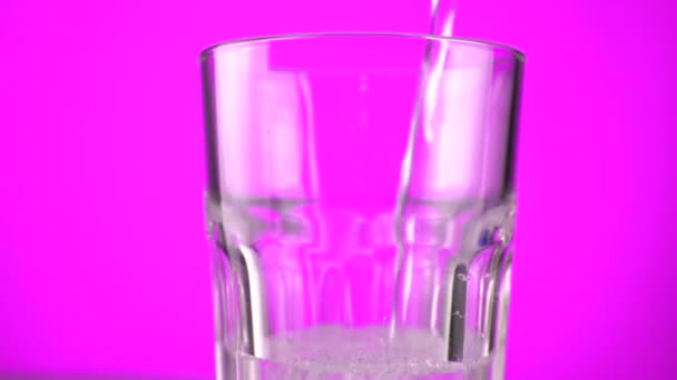 Verter agua con gas en el vaso. Rotación 360, fondo de color arco iris — Vídeo de stock