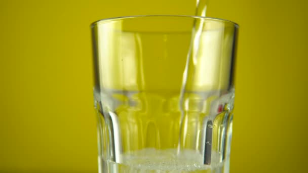 Víz öntése gázzal az ivópohárba. Rotáció 360, sárga színű háttér — Stock videók