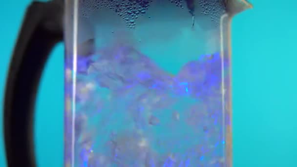 Água fervida perto na chaleira de vidro elétrica. Gire sobre fundo azul — Vídeo de Stock
