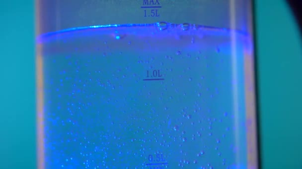 Water boiled in electric glass kettle, blue illumination. Rotate table. — Stock Video