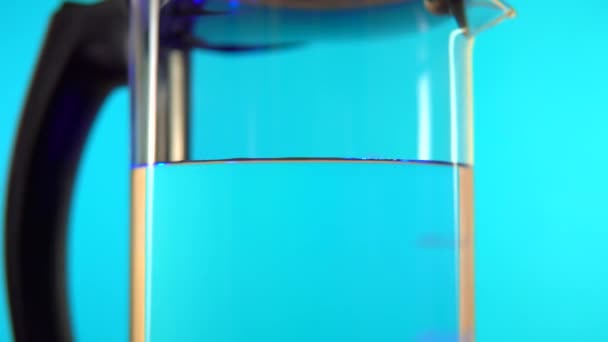 Elektrická transparentní skleněná konvice s rotací vody na modrém pozadí. — Stock video