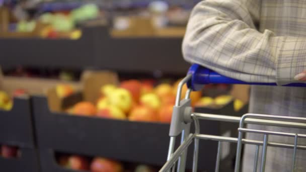 Γυναίκα περπάτημα στο σούπερ μάρκετ με τρόλεϊ ψώνια, τα χέρια πιέζει καλάθι αγορών — Αρχείο Βίντεο