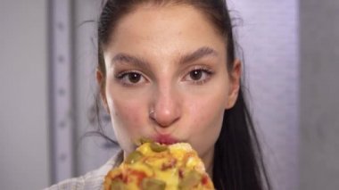 Pizza dilimleri yiyen ve kameraya bakan genç bir kadın. Yakın mesafeden pizza yiyorum. 