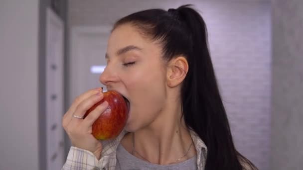 Wanita yang menarik menggigit apel merah besar, melihat kamera — Stok Video