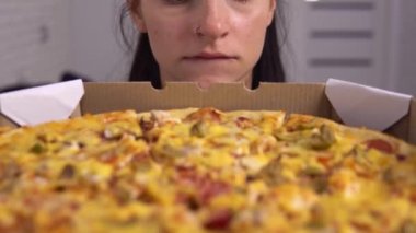 Aç diyet yapan kadın pizzaya bakıyor, dudaklarını ısırıyor. Yeme bozukluğu, açlık