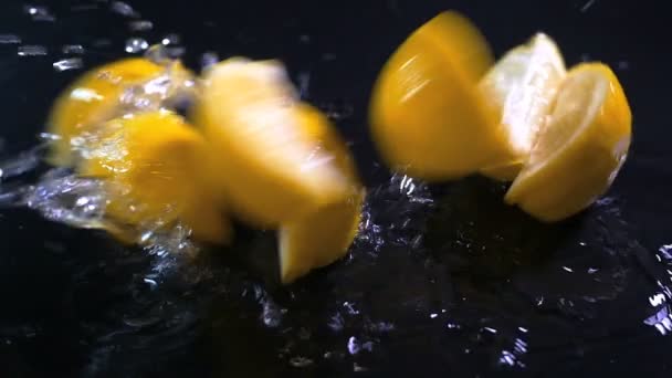 Slow motion lemon falling with water drops on black surface. — Stock Video