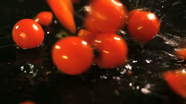 Movimiento lento de los tomates que caen con gotas de agua en la superficie negra . — Vídeo de stock