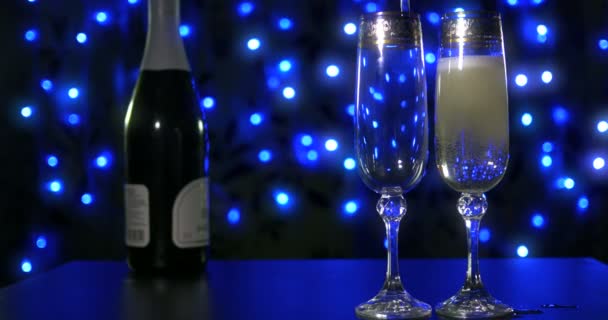 Champanhe borbulhante sendo derramado em dois copos de cristal contra boke backgroung preto — Vídeo de Stock