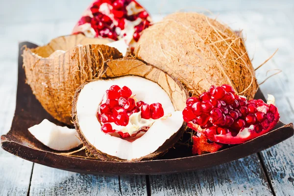 Fresh coconut and red garnet in a wooden bowl,blue background — Stock Photo, Image