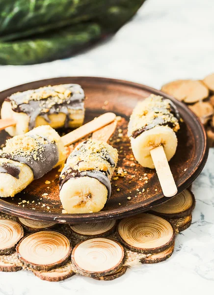 frozen bananas on a stick with chocolate and nuts, dark clay pla