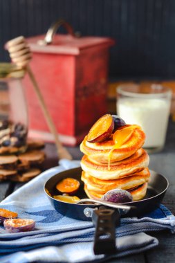 Sabah kahvaltısı. Mavi ahşap arka planda tavada tatlı erikli ve bal kaplı gözlemeler. Bir bardak süt. rustik biçim.