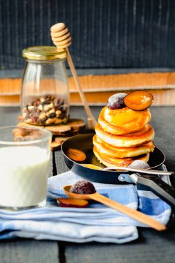 Mavi ahşap arka planda tavada tatlı erikli ve bal kaplı gözlemeler. Bir bardak süt. rustik biçim.