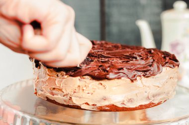 Çikolata kremalı, kremalı, yuvarlak, leziz bir pasta. Kadın eli kesiyor..