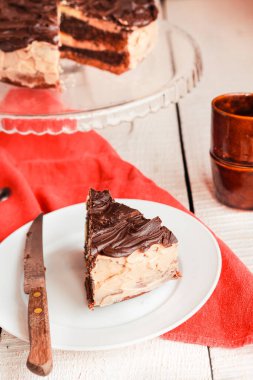 Koyu çikolatalı kek ve çikolatalı krema dilimi beyaz bir tabakta..