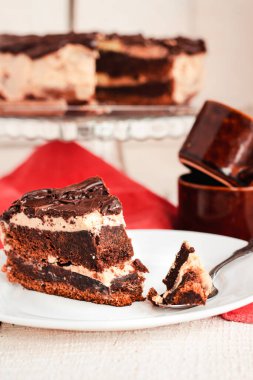 Koyu çikolatalı kek ve çikolatalı krema dilimi beyaz bir tabakta..
