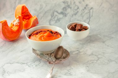 Geleneksel sonbahar ve kış yemekleri, kırmızı biberli sıcak ve baharatlı balkabağı çorbası ve mermer zemin üzerinde çavdar ekmeği. Seçici odaklanma. Boşluğu kopyala.