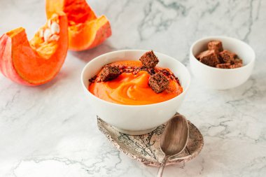 Kavrulmuş balkabağı ve havuç çorbası siyah ve kırmızı biber, mermer arka planda çavdar ekmeği. Geleneksel sonbahar ve kış yemekleri..