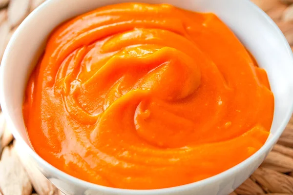 Krema bir kase portakallı kabak püre çorbasına dökülür. Sağlıklı yaşam tarzı ve sonbahar konforu. Yakın plan.