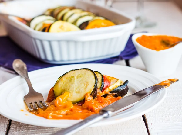 Juicy ratatouille served in a round plate with sauce, fork, knif — Stock Photo, Image