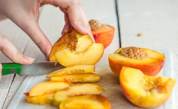 Cut ripe peach on a white board, hand — Stock Photo, Image