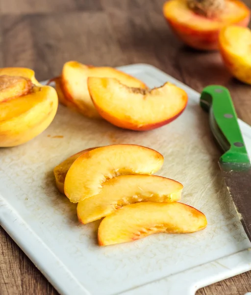 Cut slices of ripe peach on a white board, green knife — Stock Photo, Image