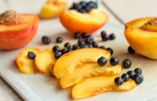 Scheiben saftige Pfirsiche und Blaubeeren auf einem weißen Brett — Stockfoto