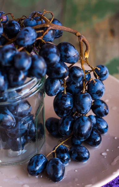 Zweig blauer Trauben im Glas auf einem Teller — Stockfoto