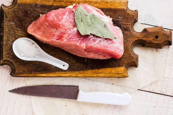 Pedazo de cerdo en una tabla de cortar, una hoja de laurel —  Fotos de Stock